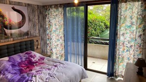 A bedroom with a bed, a headboard, a ceiling light, a window with curtains, and a view of greenery outside. - Casa Familia (La Orotava)