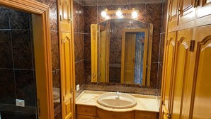 A bathroom with a marble-tiled wall, a wooden vanity with a sink, and a mirror above the vanity. - Casa Familia (La Orotava)
