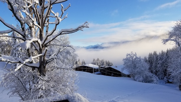 A wooden deck with snow-covered railings, a snow-covered landscape, and a building with a sloped roof in the background.