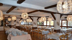 A spacious dining hall with wooden beams, round chandeliers, and tables set for multiple guests.