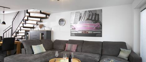 A modern living room with a grey sofa, a wooden coffee table, and a staircase with wooden railings.
