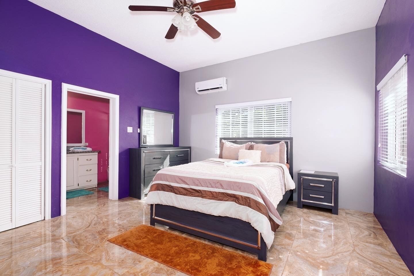 A bedroom with a bed, bedside tables, a wardrobe, a ceiling fan, and an air conditioning unit.