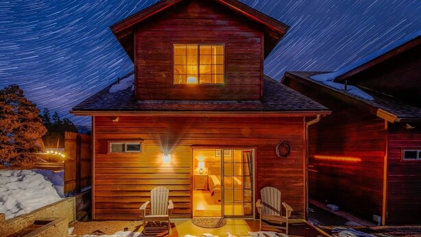 A wooden cabin with a large window and two chairs outside.