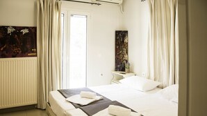 A hotel room with two beds, a radiator, a painting on the wall, and a desk with a lamp. - Villa Eros (Corfu)