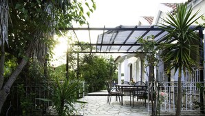 A covered patio with stone flooring, outdoor furniture, and a pergola structure. - Villa Eros (Corfu)
