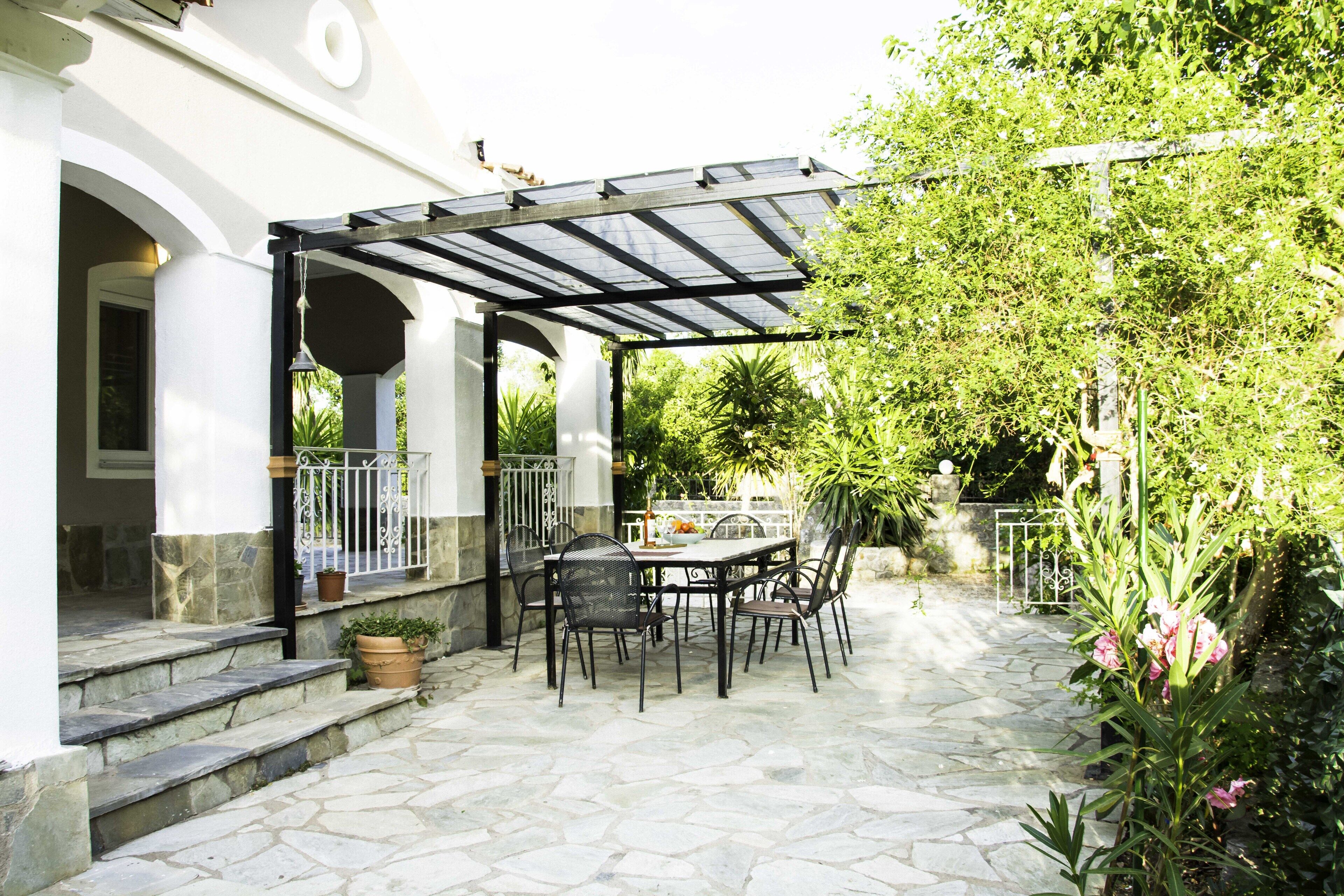 Eine Terrasse im Freien mit einer Pergola, Steinboden und einem Tisch mit Stühlen.