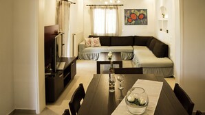 A modern living room with a dark brown sofa, a dining table with chairs, and a chandelier. - Villa Eros (Corfu)