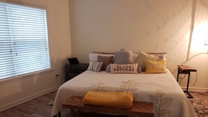 Ein Schlafzimmer mit einem Bett, Nachttisch, Lampe und einem Fenster mit Jalousien.