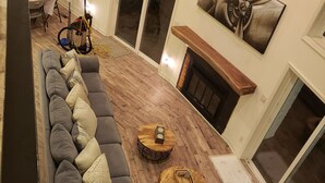 Ein geräumiges Wohnzimmer mit einem langen, grauen Ecksofa, zwei runden Couchtischen aus Holz und einem Kamin.
