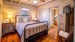 Quarto com teto de madeira, cama com roupa de cama estampada, duas mesas de cabeceira com abajures e uma cômoda de madeira.