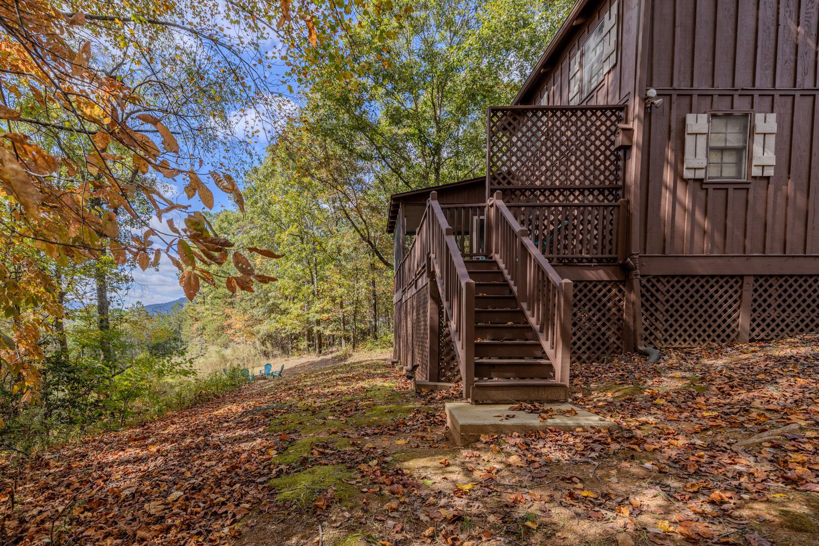 Eine Holzhütte mit einer Treppe, die zu einer Terrasse führt, umgeben von Herbstlaub und einem bewaldeten Hintergrund.