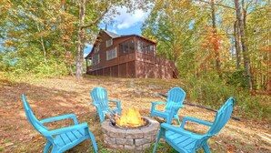 Uma cabana com um braseiro de pedra e quatro cadeiras Adirondack azuis em meio à floresta.