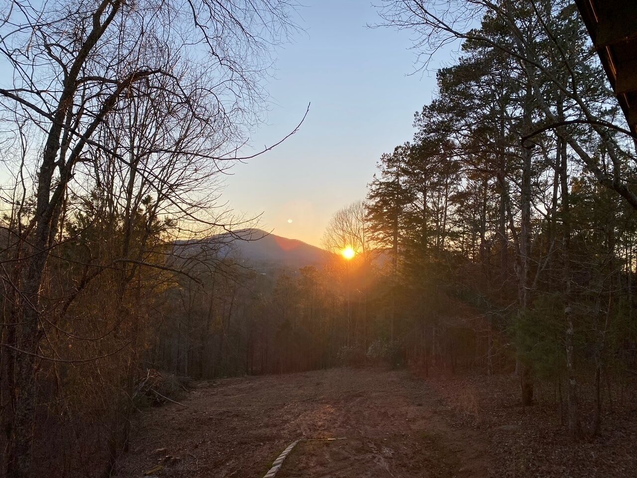 Un sendero en el bosque que lleva a una montaña, con el sol poniéndose al fondo.