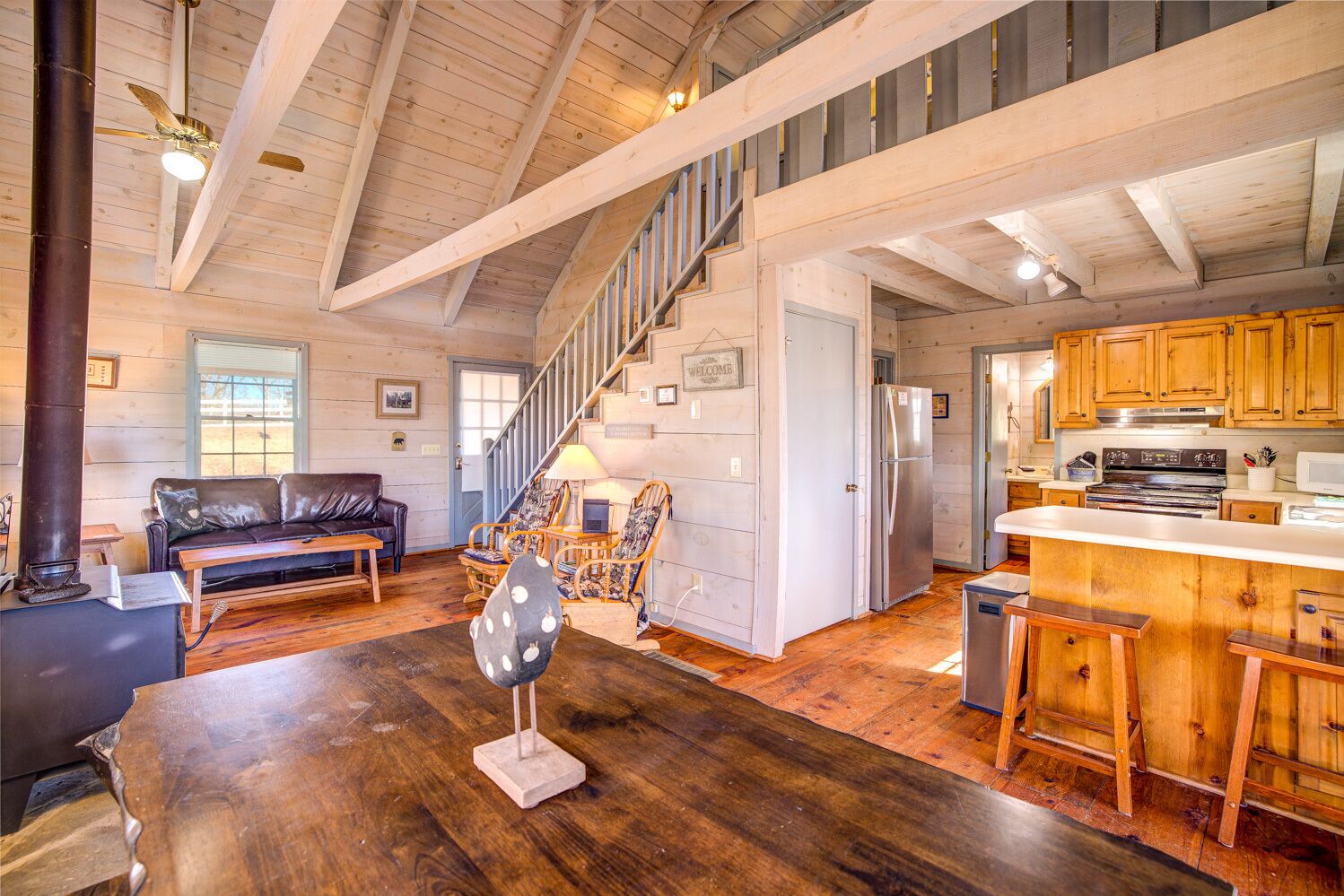 A spacious living area with a wooden floor, a black leather sofa, a wooden coffee table, and a staircase leading to an upper level.