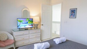 Quarto de hotel com cama, televisão mostrando uma cena de praia, cômoda, espelho e porta que dá para uma varanda.