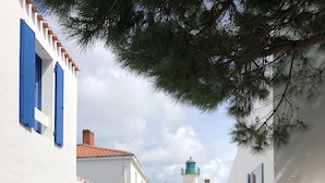 A narrow street with white buildings and blue doors, leading to a green-roofed building with a lighthouse.