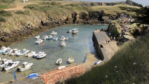 A coastal harbor with boats docked along a stone quay, surrounded by rocky cliffs and grassy terrain.