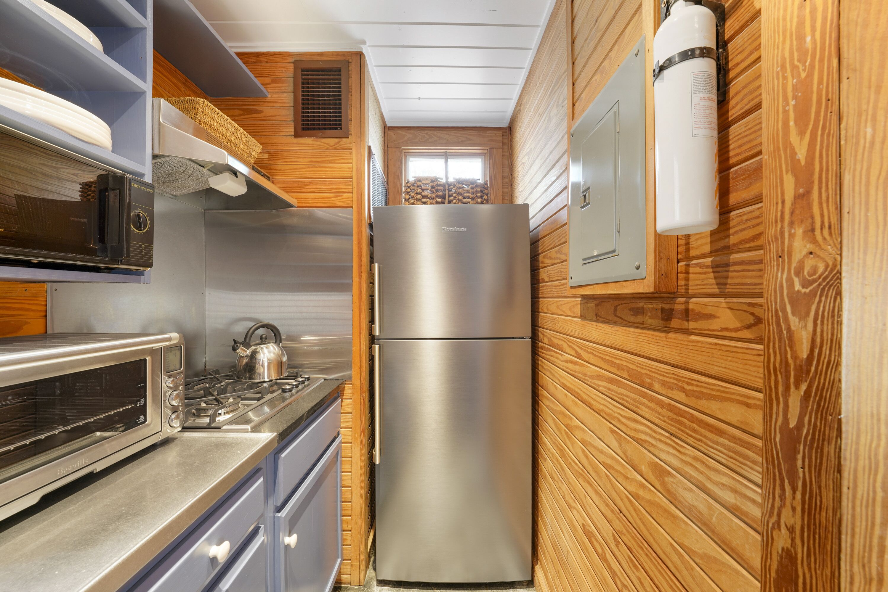 A compact kitchen with a stainless steel refrigerator, a built-in oven, and a microwave.