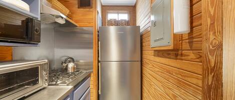 A compact kitchen with a stainless steel refrigerator, a built-in oven, and a microwave.