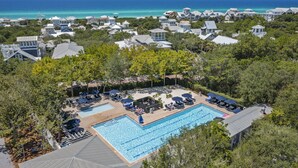 Een resort met een groot zwembad, omringd door ligbedden en parasols, met op de achtergrond de oceaan en strandhuizen.