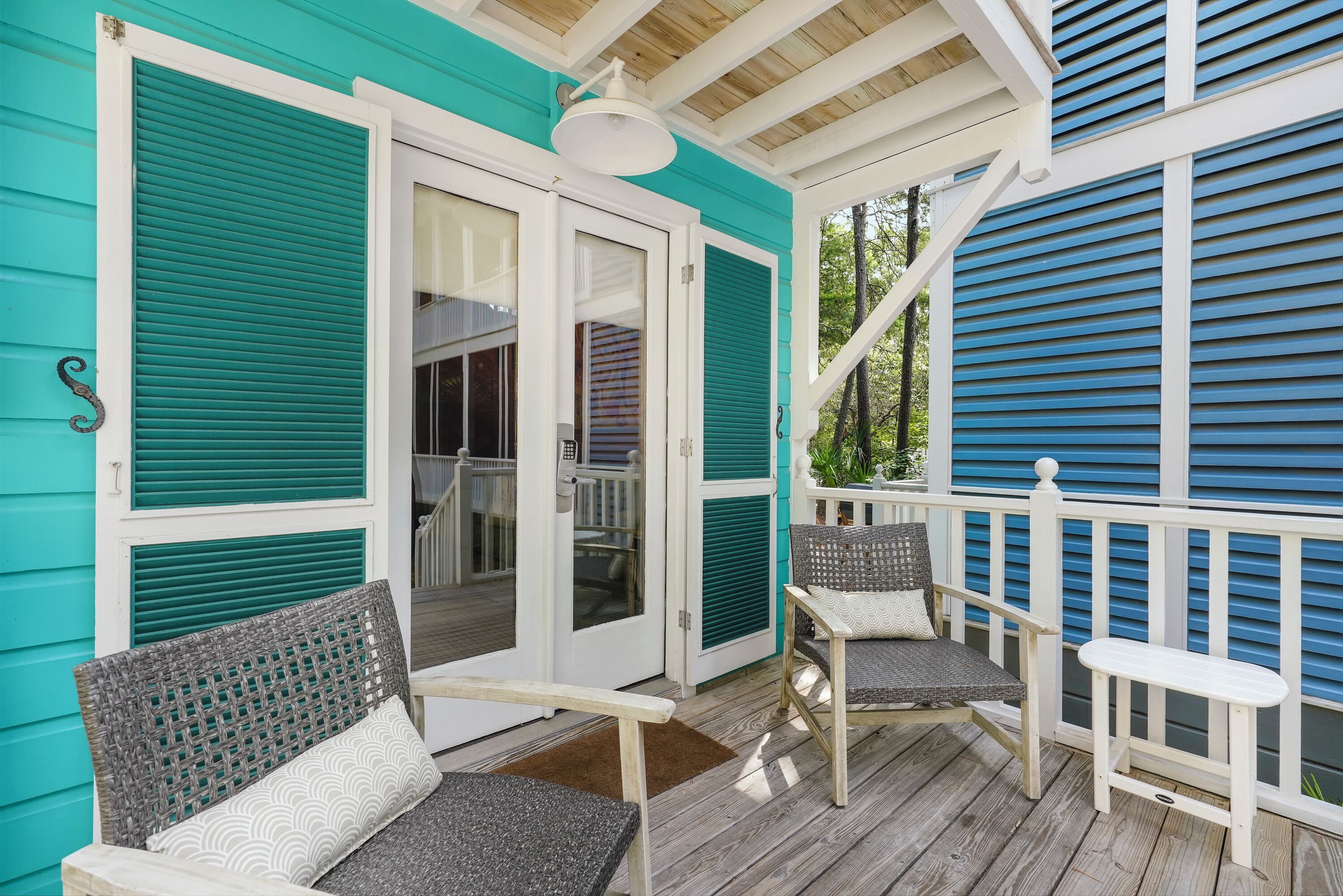 A covered porch with two wicker chairs and a small table, a sliding glass door, and a wooden deck.