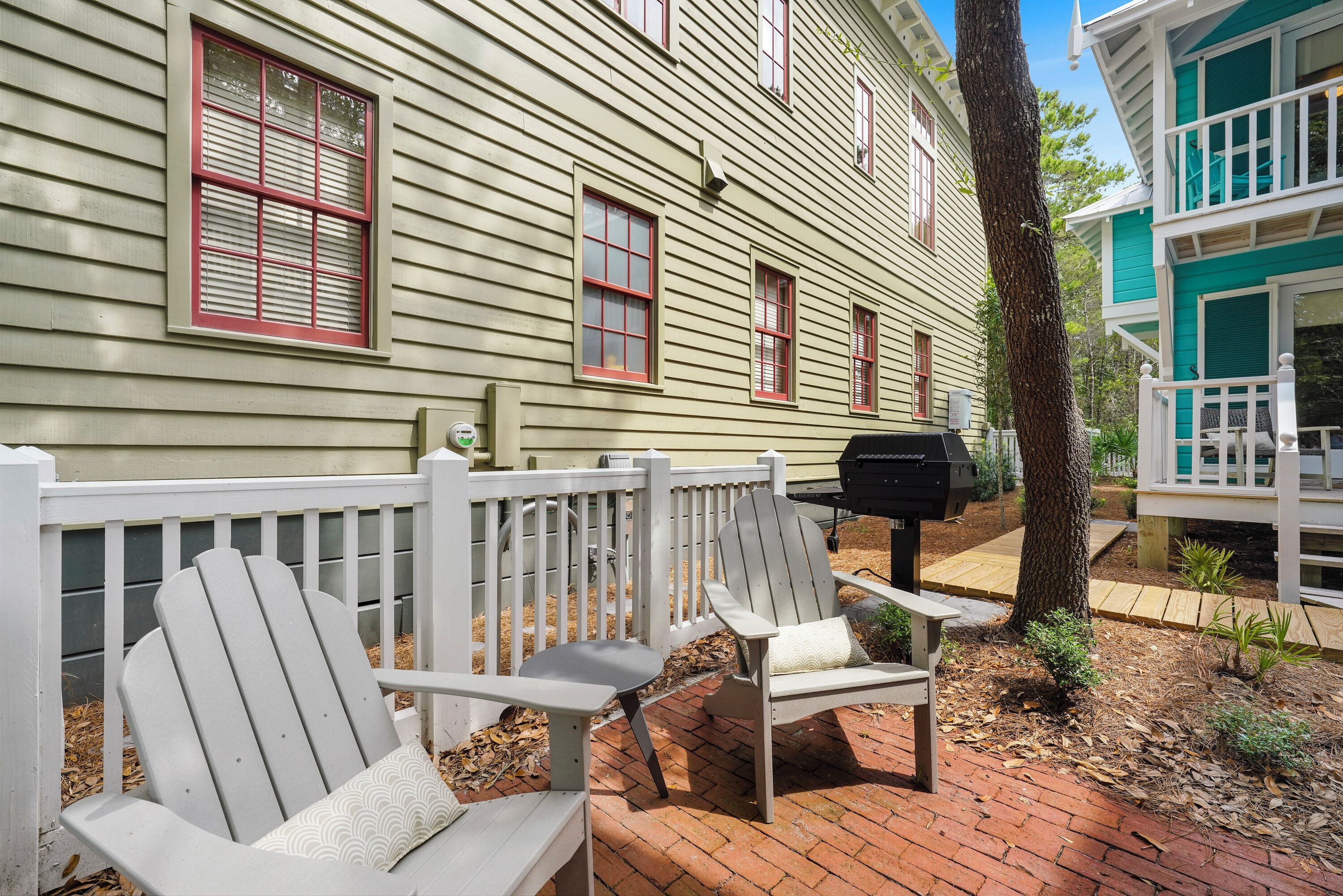 Une terrasse avec des fauteuils Adirondack, un barbecue et une clôture blanche.