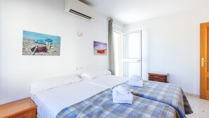 A hotel room with two beds, a wooden nightstand, a small wooden chest, and a window with a view of the sea. - A&n Moriles 2      . (Torre del Mar)