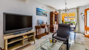A living room with a flat-screen TV, wooden furniture, a glass coffee table, and a view of a traditional building through a doorway. - A&n Moriles 2      . (Torre del Mar)