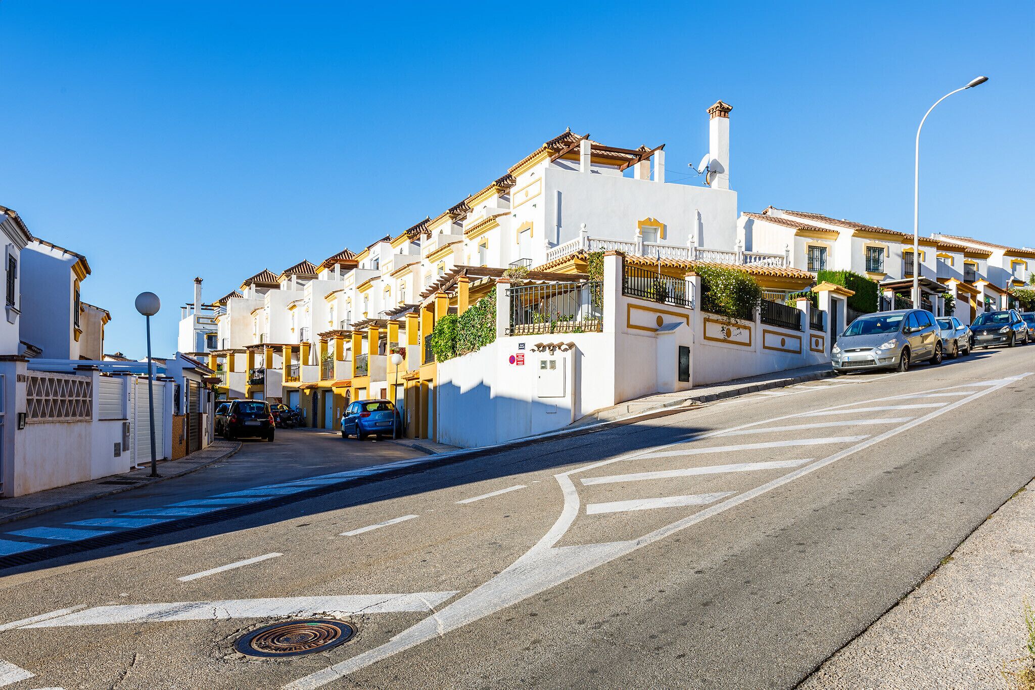 A street lined with white buildings with balconies and a clear blue sky.