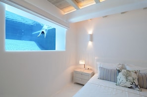 Une chambre avec une grande fenêtre, une table de chevet, une lampe et un lit avec des oreillers.