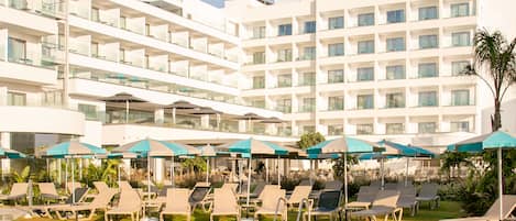 Un hotel con una piscina grande, tumbonas y sombrillas.