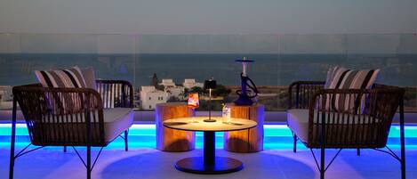 Terraço no telhado com mobiliário de vime, uma mesa redonda central e vista para o mar.