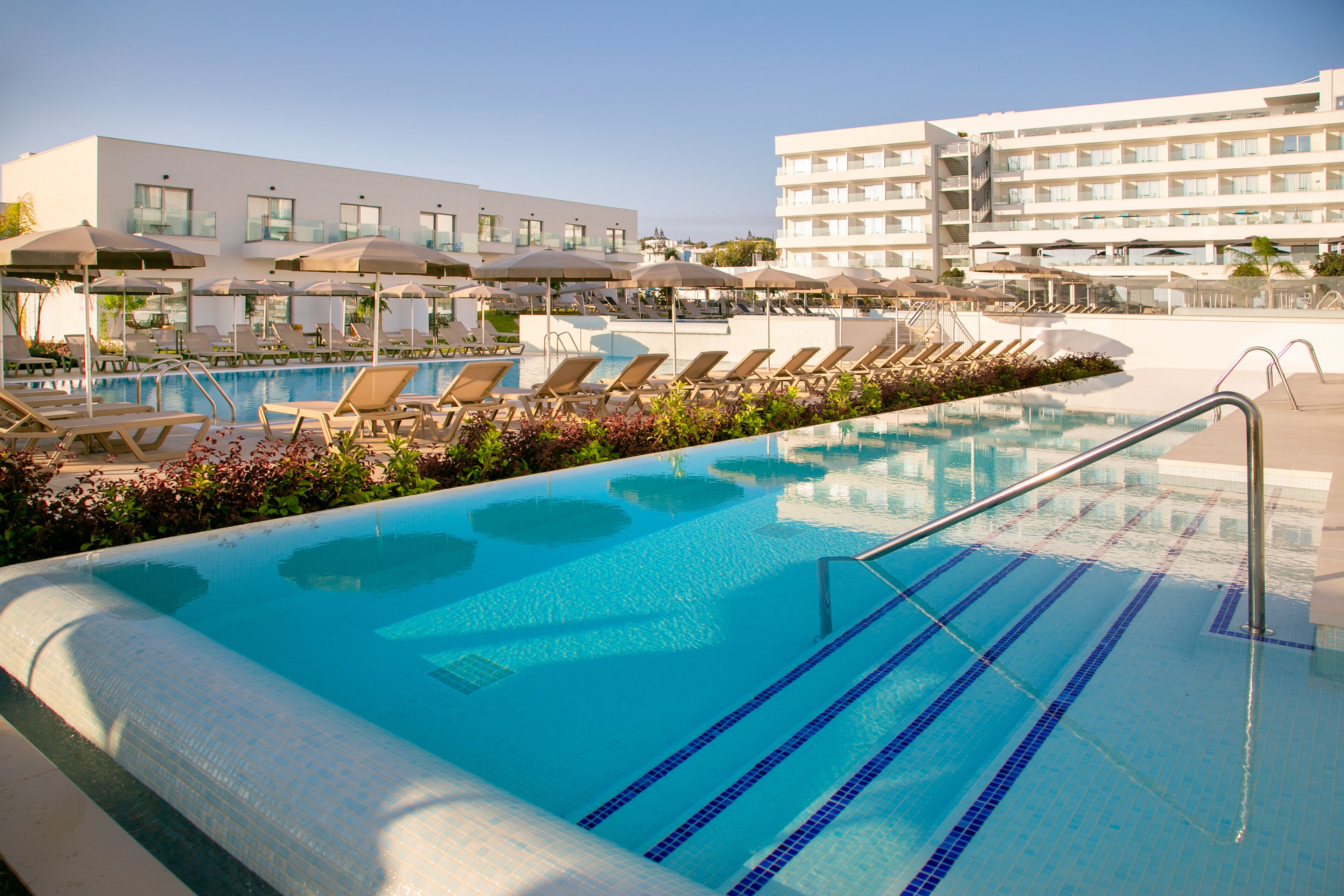 A swimming pool area with lounge chairs and umbrellas, surrounded by hotel buildings.