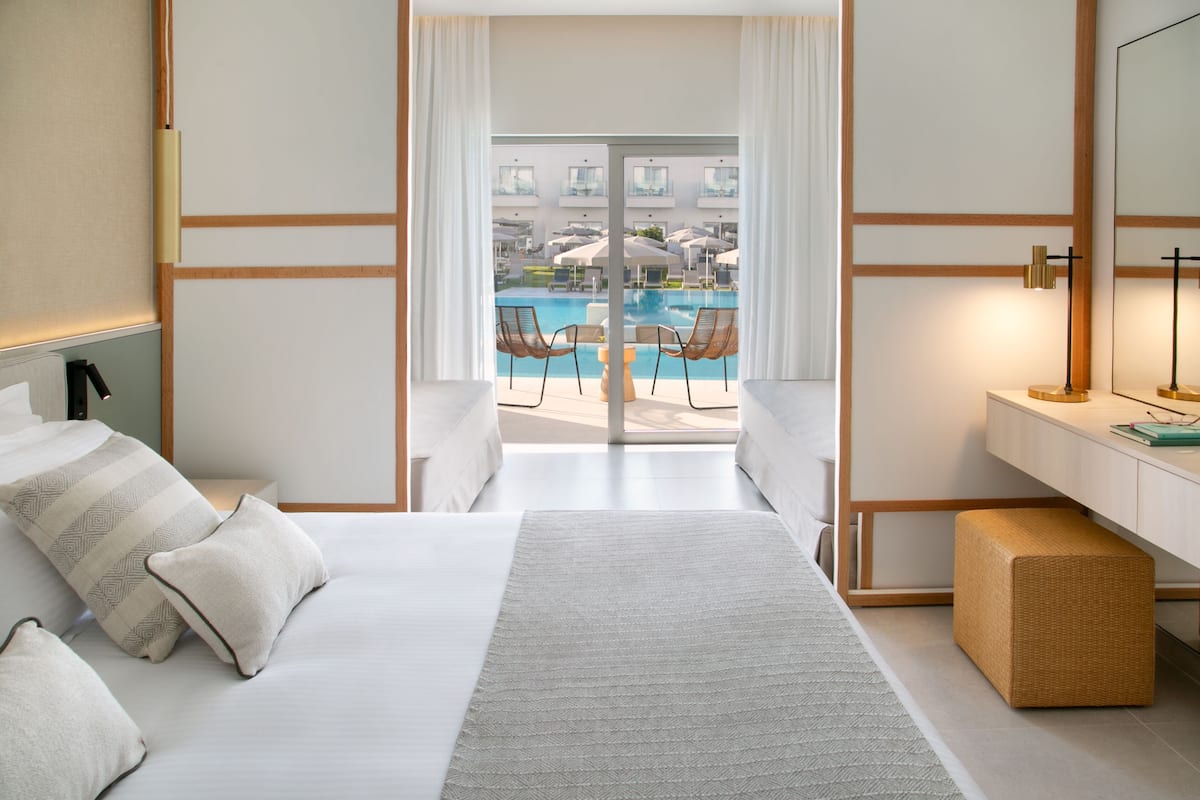 A hotel room with a large bed, a bedside table, a small side table, and a view of a pool with lounge chairs.