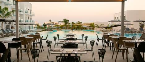 Restaurante junto a la piscina con mesas y sillas dispuestas para comer, con vistas a una piscina.