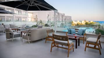 A rooftop lounge with outdoor furniture, a pool view, and a glass balustrade.