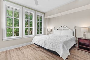 Un dormitorio con una cama grande, dos lámparas de noche, una mesita de noche y una ventana con vistas a árboles.