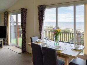 Un coin repas avec une table dressée pour deux personnes, un vase de fleurs et une vue sur la mer.