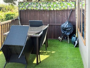 Une terrasse avec une table et des chaises, un barbecue et un tuyau d’arrosage.