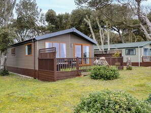 Une petite maison mobile d’un seul étage, dotée d’une terrasse clôturée et entourée d’arbres et d’herbe.