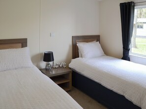 A twin room with two beds, a nightstand with a lamp, and a window with curtains. - Ocean Glade - UK32963 (Corton, near Lowestoft)