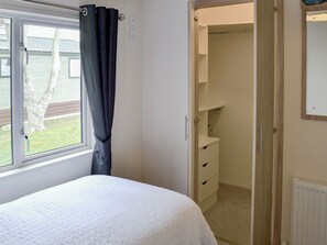 A bedroom with a bed, a window with curtains, a closet with shelves, and a radiator.