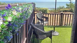 A deck with a view of the ocean, a red umbrella, and wicker chairs. - Ocean Glade - UK32963 (Corton, near Lowestoft)