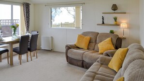 A living room with a sofa, chairs, a dining table, and a window with a view. - Ocean Glade - UK32963 (Corton, near Lowestoft)