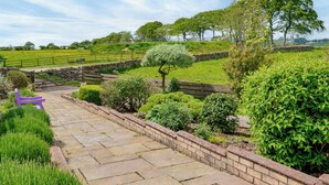 A stone pathway leading to a purple bench in a lush garden with a stone wall and a view of a green field. - 2 bedroom accommodation in Lochmaben near, Lockerbie (Lochmaben near, Lockerbie)
