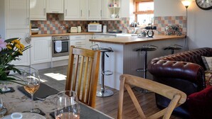 A modern kitchen with white cabinetry, a central island with stools, a dining area with a table set for two, and a leather sofa in the living area. - 2 bedroom accommodation in Lochmaben near, Lockerbie (Lochmaben near, Lockerbie)