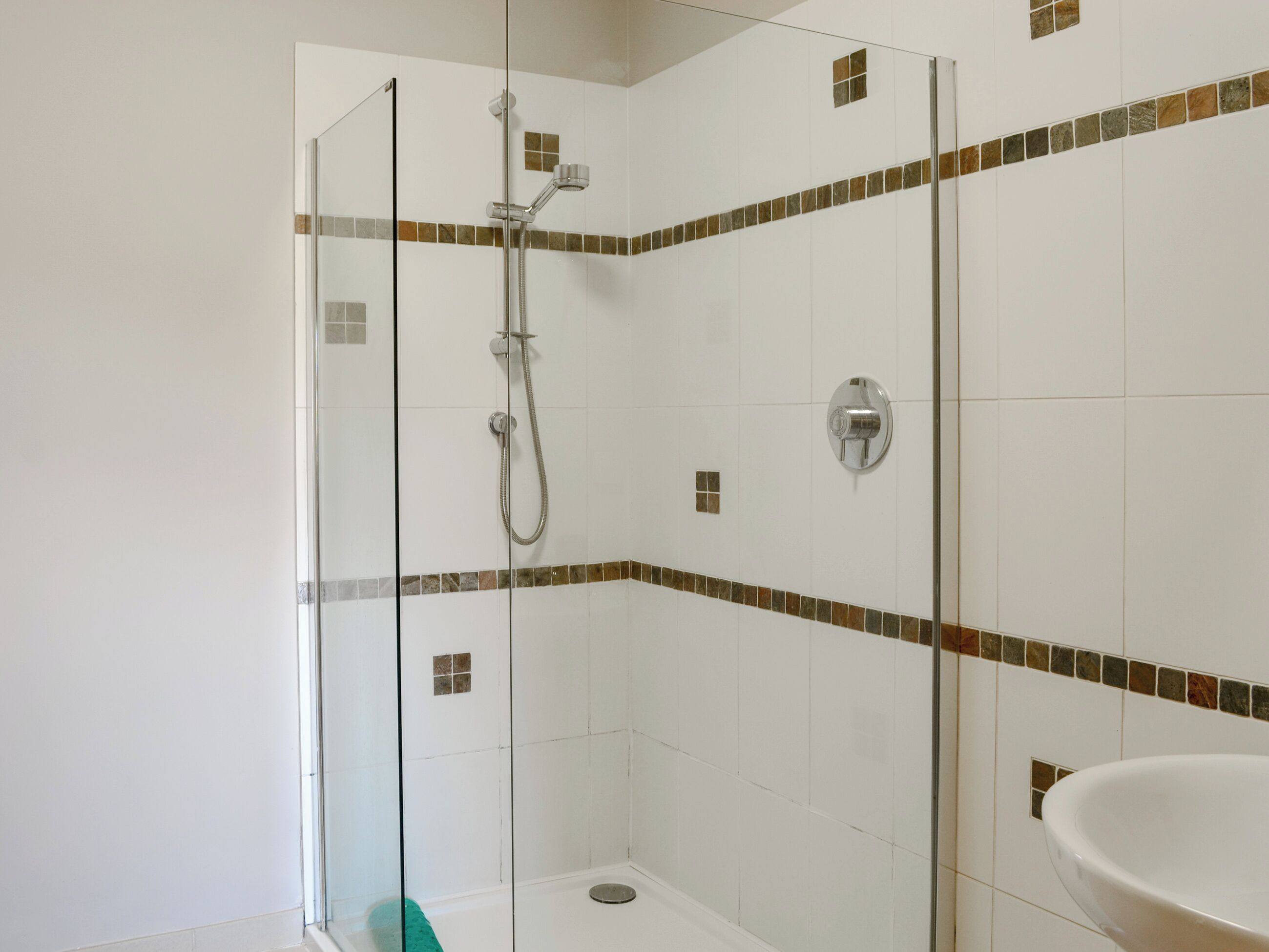 Une douche avec une porte en verre, un espace de douche carrelé et un lavabo avec un receveur.