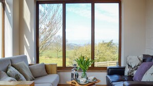 A living room with a large window, a sofa, a coffee table, and a leather armchair. - 2 bedroom accommodation in Lochmaben near, Lockerbie (Lochmaben near, Lockerbie)