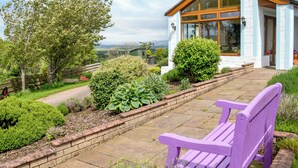 A purple bench in a garden with a view of a house with a large window and a wooden roof. - 2 bedroom accommodation in Lochmaben near, Lockerbie (Lochmaben near, Lockerbie)