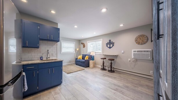 Una cocina moderna con armarios azules, horno empotrado y refrigerador. Hay un comedor con sofá y dos taburetes de bar.